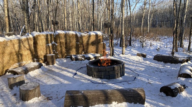 Fire pit, tree trunk seats around it and hay bales to one side.